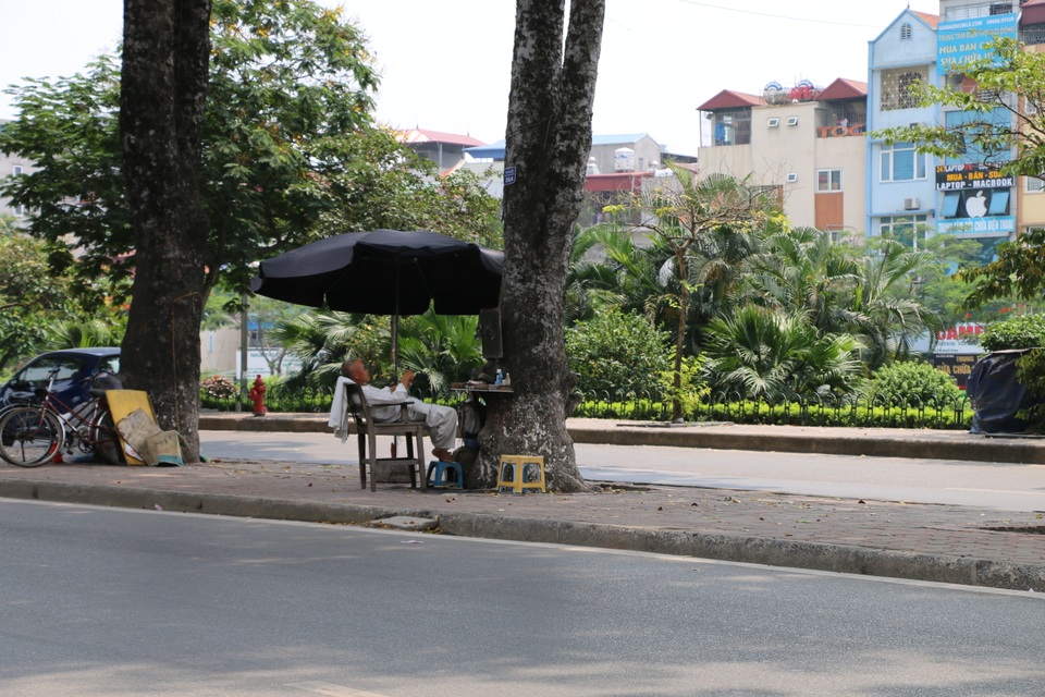 Nhọc nhằn những giấc ngủ trưa dưới nắng nóng của người lao động - 8 Dưới bóng cây xà cừ cổ thụ ở vỉa hè đường Láng, những quán cắt tóc vỉa hè còn mở thêm ô dù để tránh bớt cái nắng nóng của mùa hè đang đến.