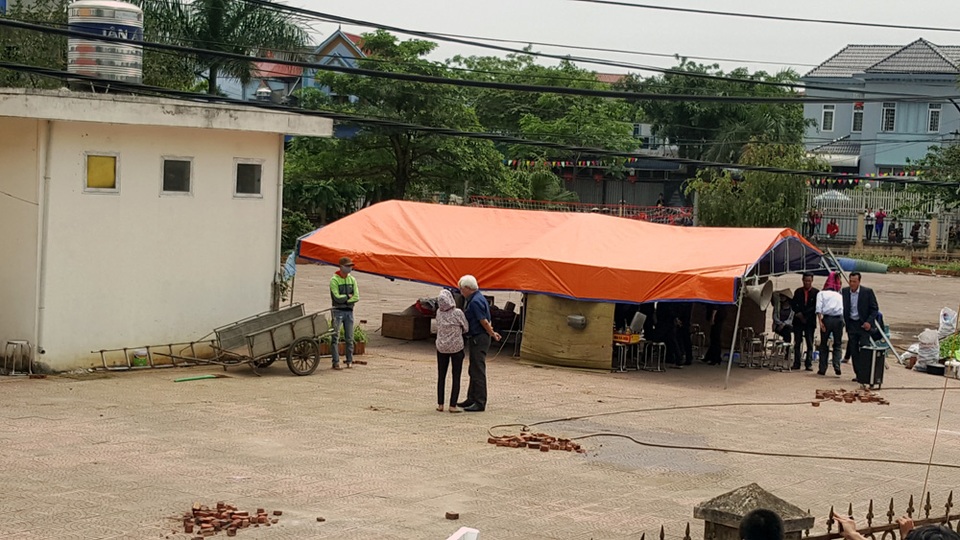 Đoàn công tác và đại diện người dân làm biên bản bàn giao tại lán được dựng trong sân nhà văn hóa. Ông Dương Trung Quốc (áo xanh) cũng có mặt, trò chuyện cùng người dân.