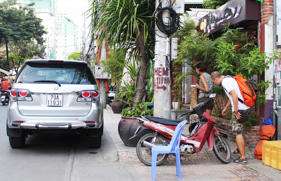 2 du khách nước ngoài chật vật lòn qua một khoảng hở khá nhỏ bé trên vỉa hè ở đường Hùng Vương