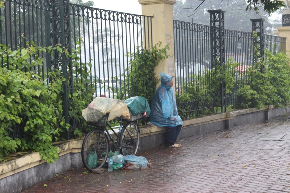 Người đàn ông sửa xe dạo ngồi co ro bên đường trú cơn mưa to và không quên che chắn cẩn thận cho đồ nghề của mình.