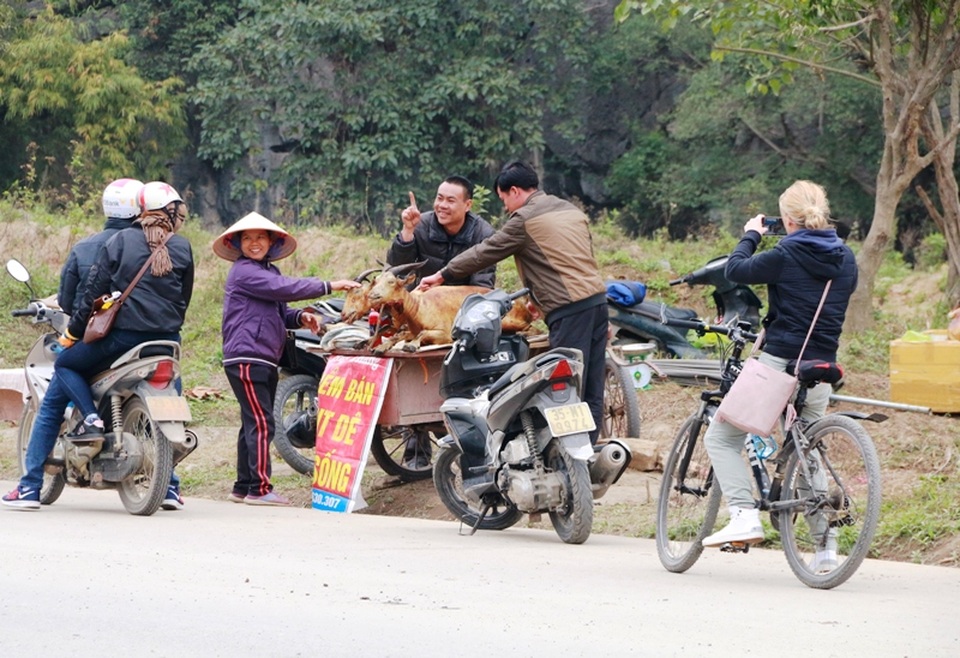 Một du khách nước ngoài dùng máy ảnh ghi lại cảnh bán thịt dê ven đường của người dân Ninh Bình