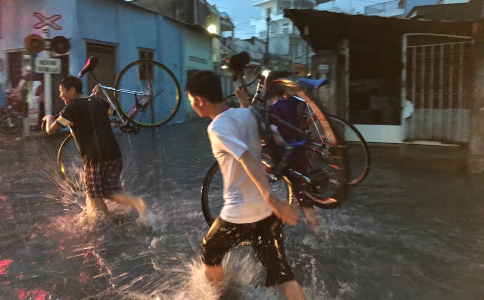 Nhiều thiếu niên vác xe đạp vượt qua vùng ngập nước và kẹt xe để về nhà.