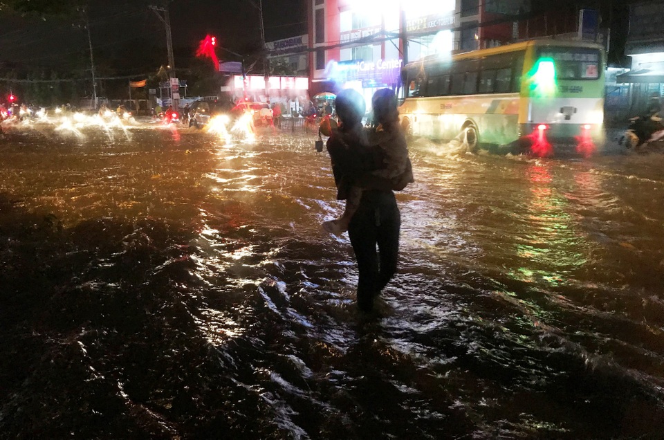 Hồ điều tiết chống ngập lại “thất thủ” trong cơn mưa lớn - 5 Một người mẹ bồng con nhỏ bì bõm lội qua vùng ngập nước trên đường Võ Văn Ngân để đón xe buýt về nhà.