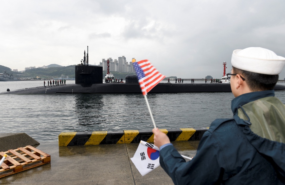 Một binh sĩ cầm cờ Hàn Quốc và Mỹ chào đón tàu ngầm USS Michigan cập cảng Busan (Ảnh: Reuters)