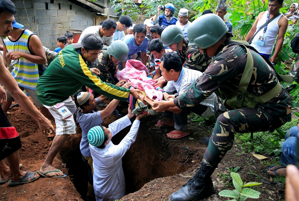 Philippines dốc sức giải phóng thành phố bị phiến quân chiếm đóng - 5 Giới chức Philippines cho biết ngoài hàng trăm phiến quân của nhóm Maute, đối đầu với quân đội chính phủ tại Marawi hiện nay còn có 40 tay súng nước ngoài tới yểm trợ. Các phiến quân thậm chí còn tích trữ lương thực cũng như vũ khí trong các nhà dân, nhà thờ, trường học cũng như mạng lưới đường hầm dưới lòng đất để chuẩn bị cho một cuộc chiến dài ngày. Trong ảnh: Các binh lính hỗ trợ người dân mai táng thi thể một nạn nhân thiệt mạng trong các cuộc giao tranh tại Marawi.