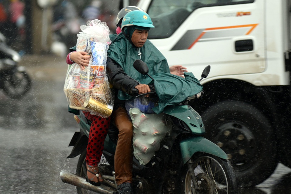 Cơn mưa lớn bất ngờ đổ xuống khiến việc di chuyển của người dân gặp khó khăn. Những người mang vác quà bánh, hành lí nặng đành chấp nhận ướt người để lấy áo mưa che đồ đạc.