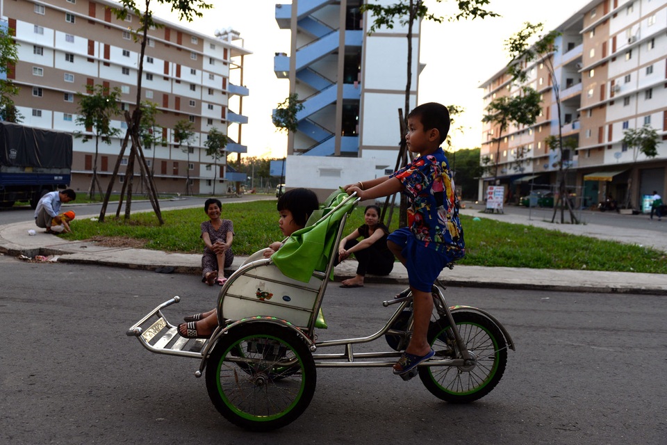 Trẻ em chơi trò chơi, người lớn ngồi hóng mát ở bãi cỏ bên trong khuôn viên khu dân cư.