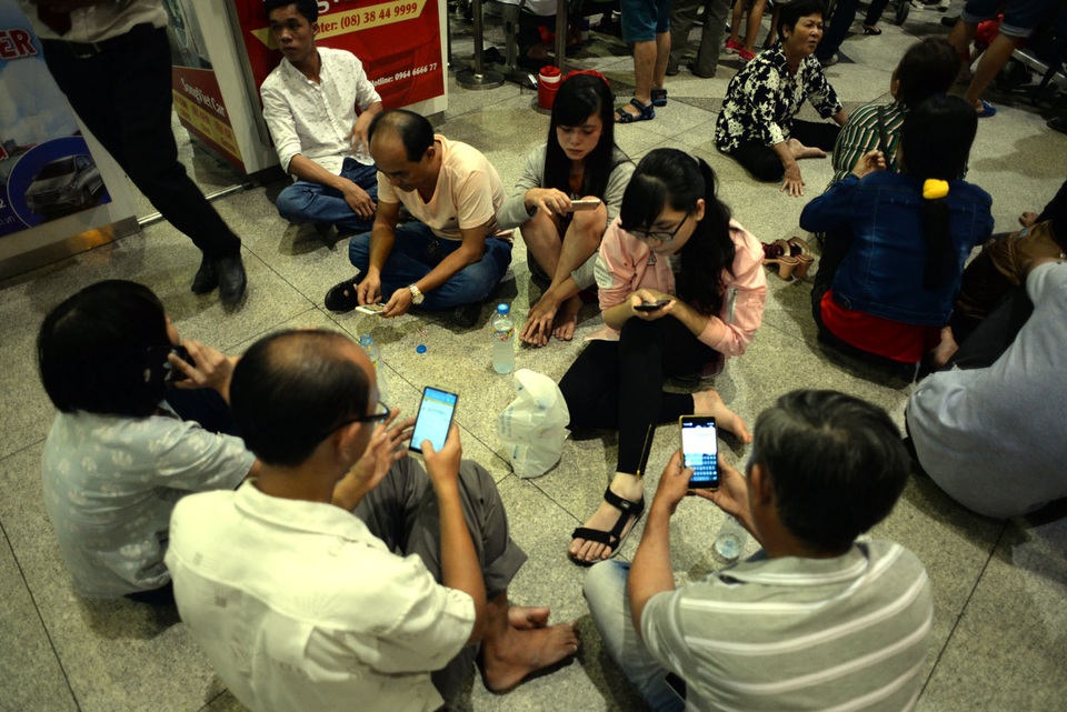 Muôn kiểu ngủ vật vờ ở sân bay chờ đón người thân về Tết - 11 Người lớn xài điện thoại để giữ tỉnh táo, chờ đón người thân.