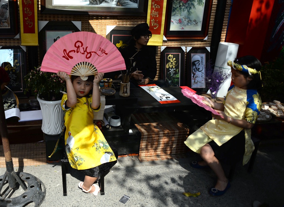 Hai em bé tạo dáng trước bàn viết thư pháp của ông đồ.