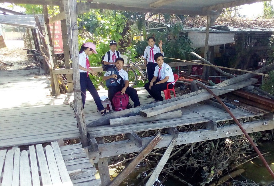 Các em học sinh ngồi đợi bạn ở một góc cầu gỗ đã được tháo dỡ do bão số 12