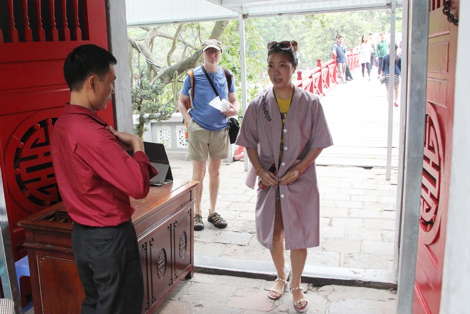 Người mặc váy ngắn, quần cộc phải khoác áo choàng khi vào đền Ngọc Sơn - 10 Nhân viên Ban quản lý nhắc nhở du khách cài khuy áo choàng khi vào đền Ngọc Sơn.