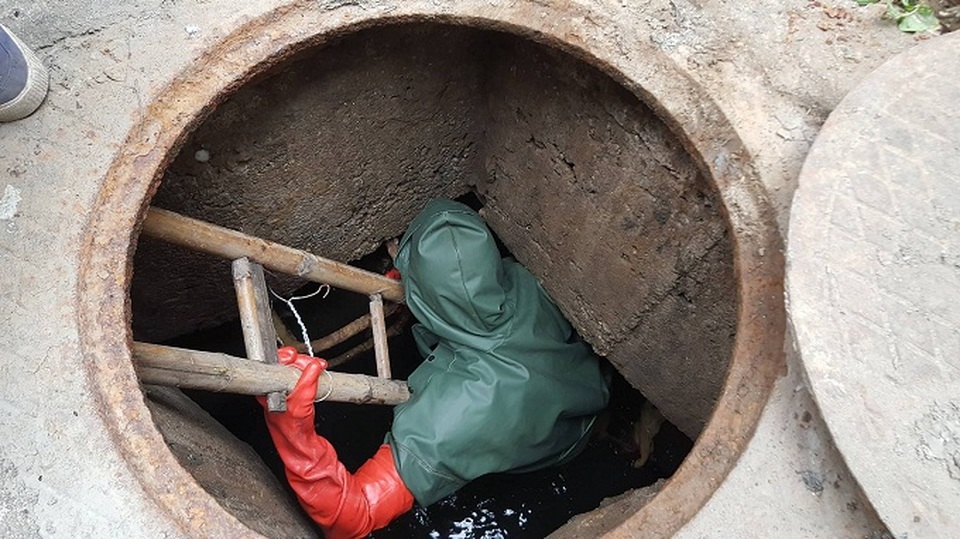 Một công nhân đnag chui xuống lòng cống đen kịt, thực hiện công việc nạo vét cống (Ảnh: Nhật Linh)