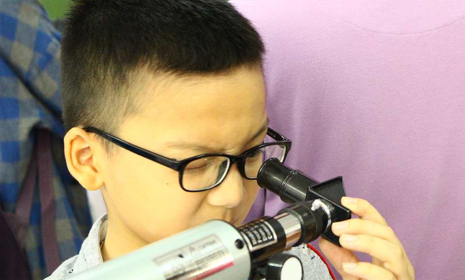 Một bạn nhỏ chăm chú quan sát kính thiên văn.