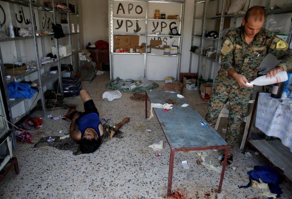 Bên trong bệnh viện dã chiến ở “chảo lửa” Syria - 4 Do không có giường bệnh nên các binh sĩ bị thương phải nằm trên một bàn dài hoặc nằm trực tiếp trên sàn nhà trong lúc điều trị tại bệnh viện dã chiến ở Raqqa.