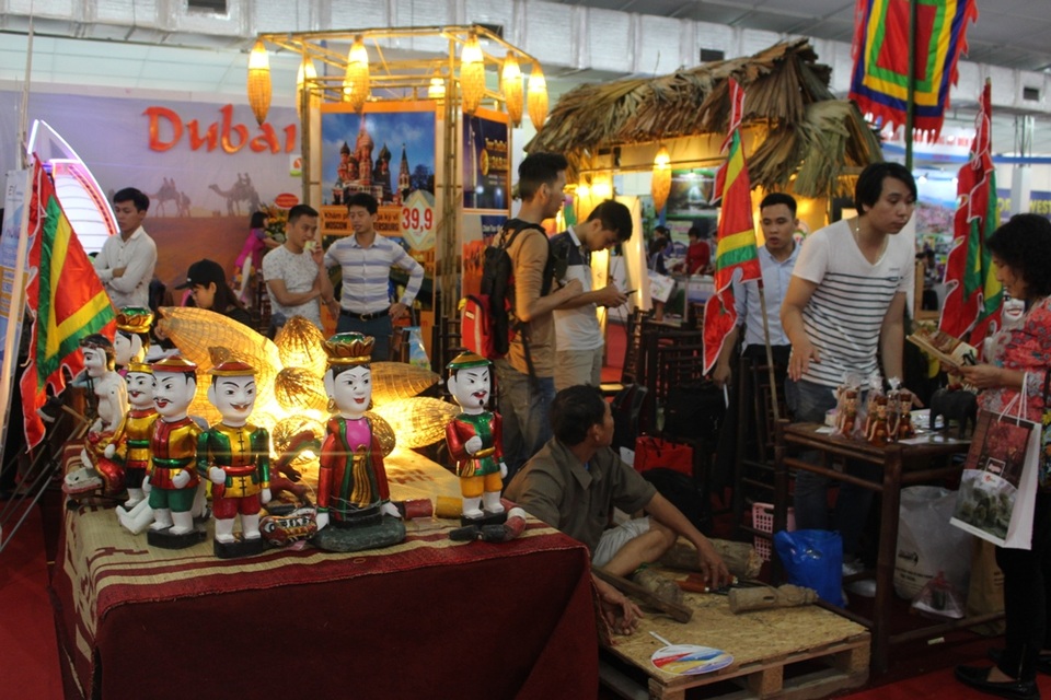 Mội gian hàng tái hiện không gian múa rối nước với các con rối làm bằng gỗ mít, cánh cổng làng quê và một nghệ nhân đang đục, tạo hình rối.