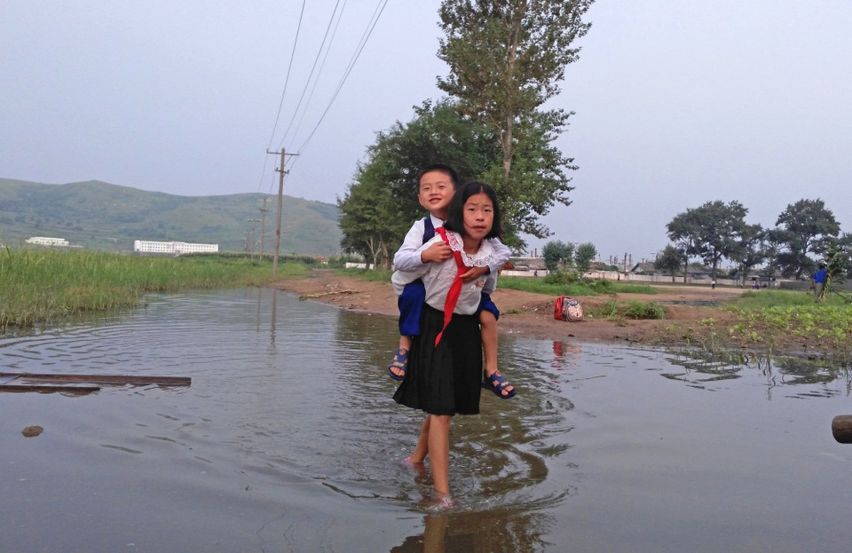 Góc nhìn hiếm có về Triều Tiên từ ô cửa tàu hỏa - 7 Hai em nhỏ Triều Tiên cõng nhau qua vũng nước.