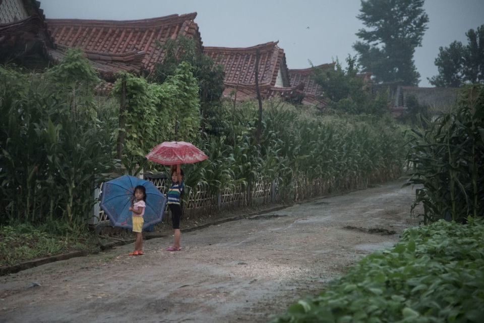 Muôn màu cuộc sống ngày hè ở Triều Tiên - 17 Hai em nhỏ đứng dưới mưa tại một ngôi làng ở ngoại ô Sinchon, phía nam Bình Nhưỡng.