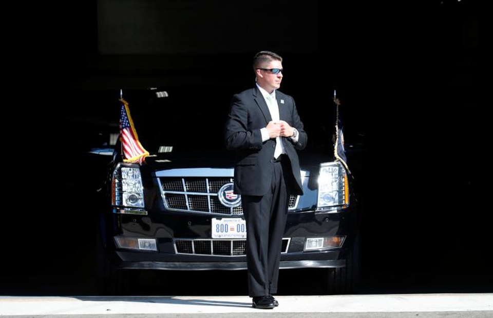 Mọi sự kiện Tổng thống Trump tham gia đều có “bóng dáng” của Mật vụ. Đặc điểm nhận dạng thường thấy của Mật vụ Mỹ là đeo kính đen và gắn thiết bị nghe sau gáy. Trong ảnh: Mật vụ đứng bảo vệ xe trước mũi xe tổng thống khi ông Trump tới thăm Trường Công nghệ Waukesha ở Pewaukee, bang Wisconsin hôm 13/6.