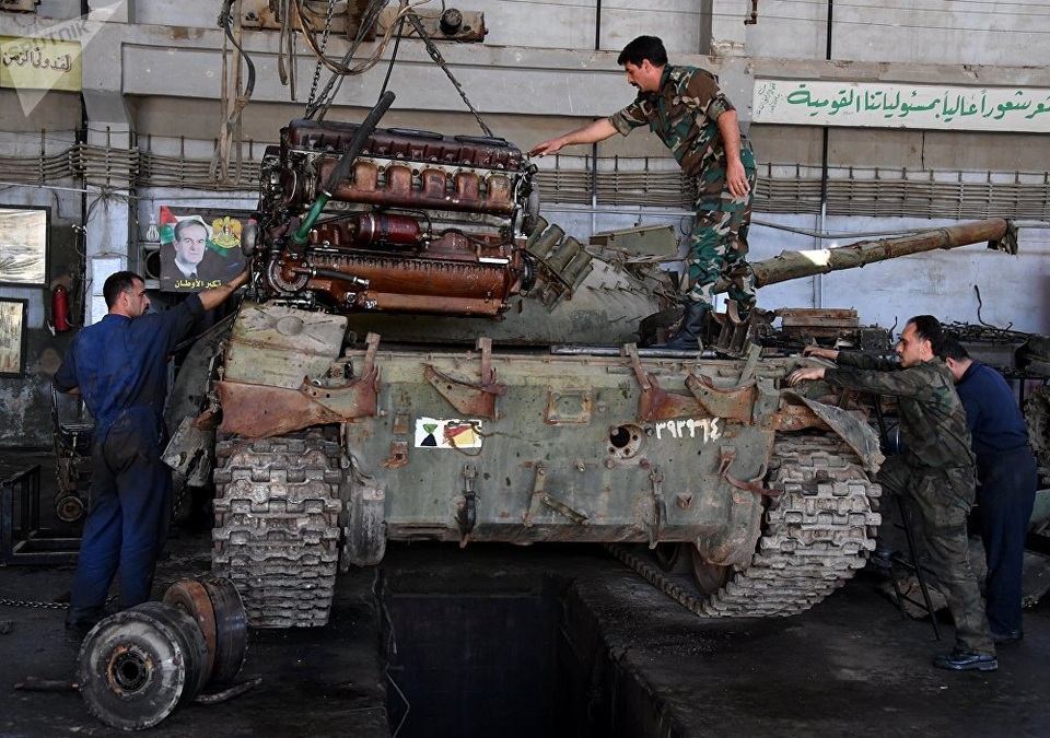 Cận cảnh nơi “hồi sinh” xe tăng cho các trận chiến ở Syria - 1 Theo Sputnik, mặc dù chiến sự vẫn đang diễn ra ác liệt tại nhiều khu vực ở Syria nhưng tại những khu vực do chính phủ kiểm soát, sự tồn tại của những nhà máy công nghiệp chưa bị chiến tranh tàn phá đã giúp chính quyền Damascus tiếp tục nuôi hy vọng về việc “tái sinh” sức mạnh chiến đấu. Trong ảnh: Các công nhân đang lắp đặt một động cơ mới vào một xe tăng quân sự tại nhà máy sửa chữa xe tăng và xe bọc thép ở Damascus.