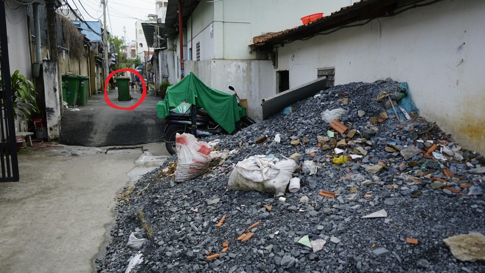 Đống xà bần ông Hòa gom về chuẩn bị cho việc nâng nền. Phía xa, chỗ vị trí khoanh tròn là miệng hố ga điều tiết nước cho máy bơm được người dân đánh dấu bằng thùng rác