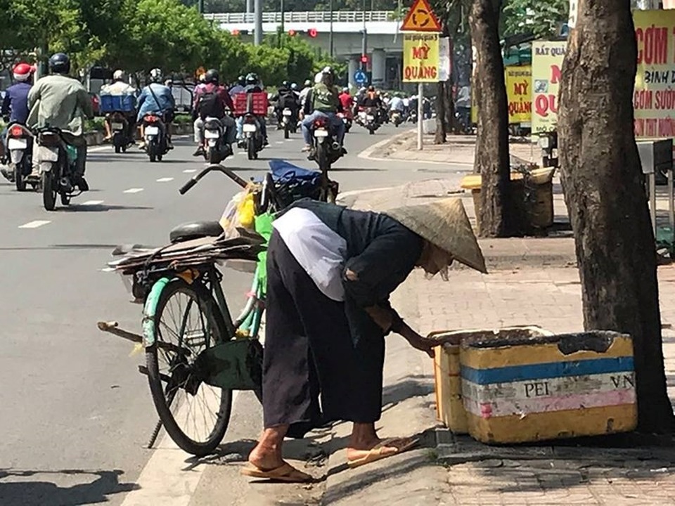 Bà già ve chai liêu xiêu giữa dòng đời bất tận - 2 Vừa dắt xe đi chầm chậm, cụ vừa tranh thủ lượm ve chai trong những thùng rác ven đường. Ảnh: VIỆT HOA