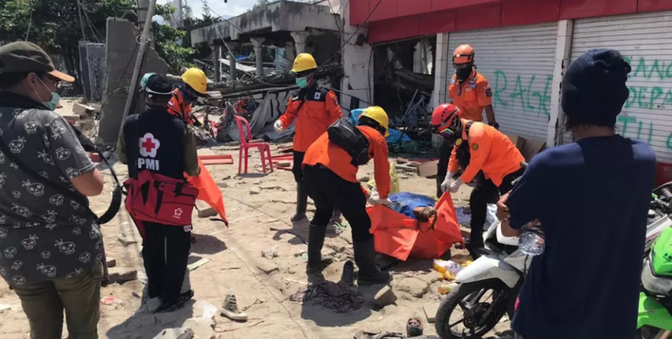 Các tình nguyện viên đặt thi thể một phụ nữ tại cửa hàng ở Talise vào túi xác. (Ảnh: Amilia Rosa)