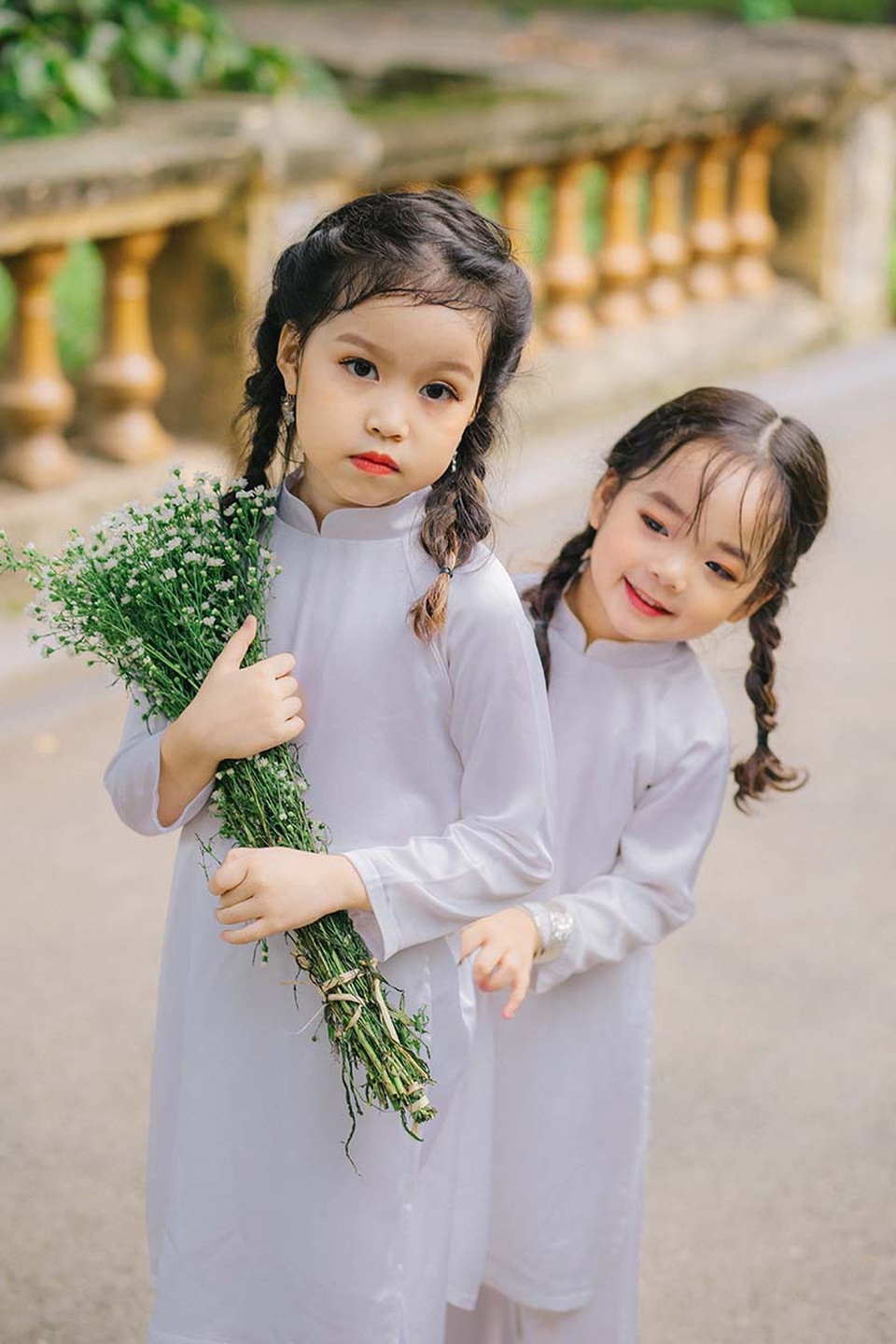 Cặp chị em mẫu giáo xinh như thiên thần - 4 Trong trang phục áo dài trắng, hai thiên thần nhí khiến người đối diện không thể nào không yêu. Các bé bên những bó cúc họa mi thuần khiết, vui đùa và chuyện trò như những người bạn. Thủy Minh lúc nào cũng tỏ ra là một cô chị biết quan tâm và chăm sóc Thủy Tiên.