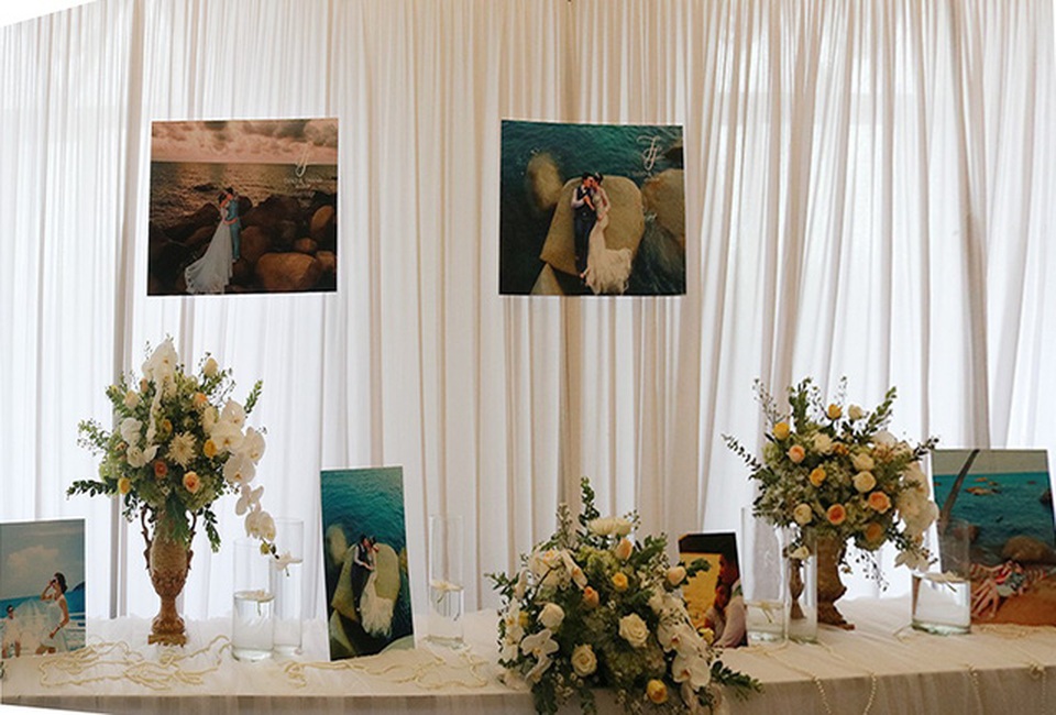 Không gian tiệc cưới cũng được chọn tông trắng chủ đạo, trang trí bằng hoa tươi sang trọng cùng ảnh cưới ngọt ngào mà cặp đôi đã chụp trước đó.