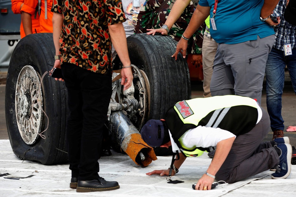 
Các nhân viên kỹ thuật kiểm tra phần bánh máy bay vớt được từ dưới biển.
