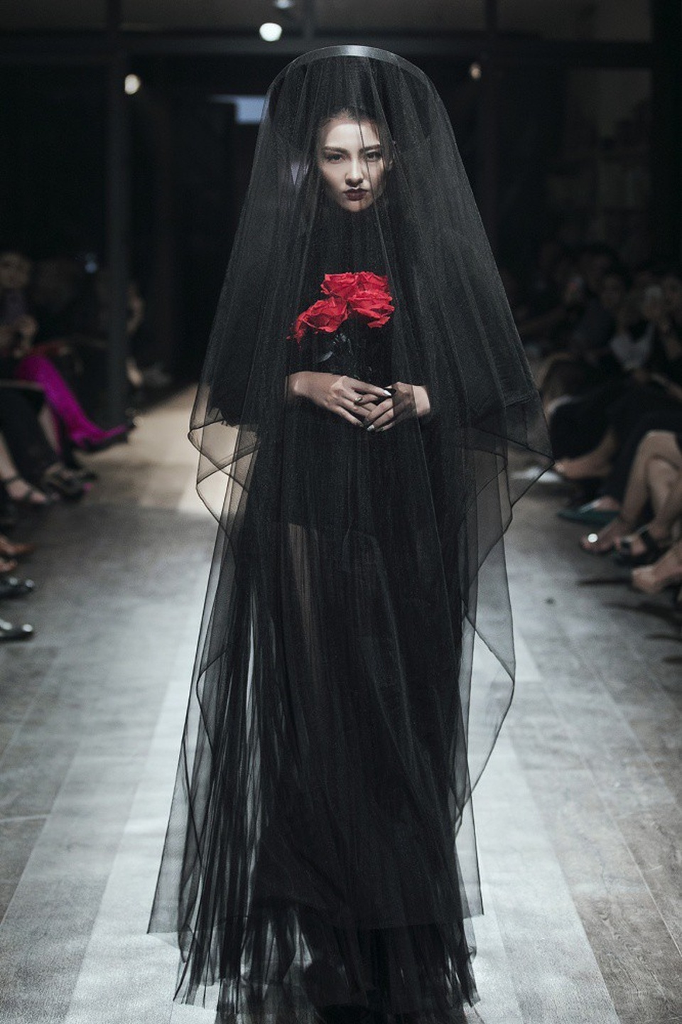 Hồng Quế uy quyền bước ra đường băng với bộ đồ đen huyền bí, ôm bó hoa hồng đỏ rực trong tay. Cô đội mấn, che mạng, bộ đồ xuyên thấu giúp Hồng Quế khoe trọn vòng 3 bốc lửa.