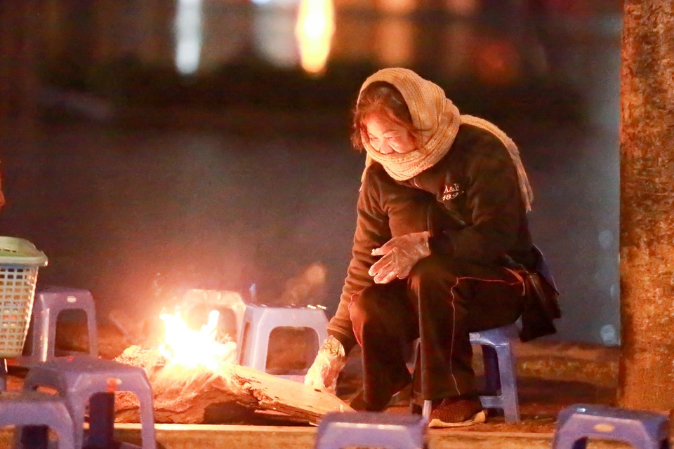 
Một người bán nước bên đường đang đốt lửa sưởi ấm ngoài trời gió rét.
