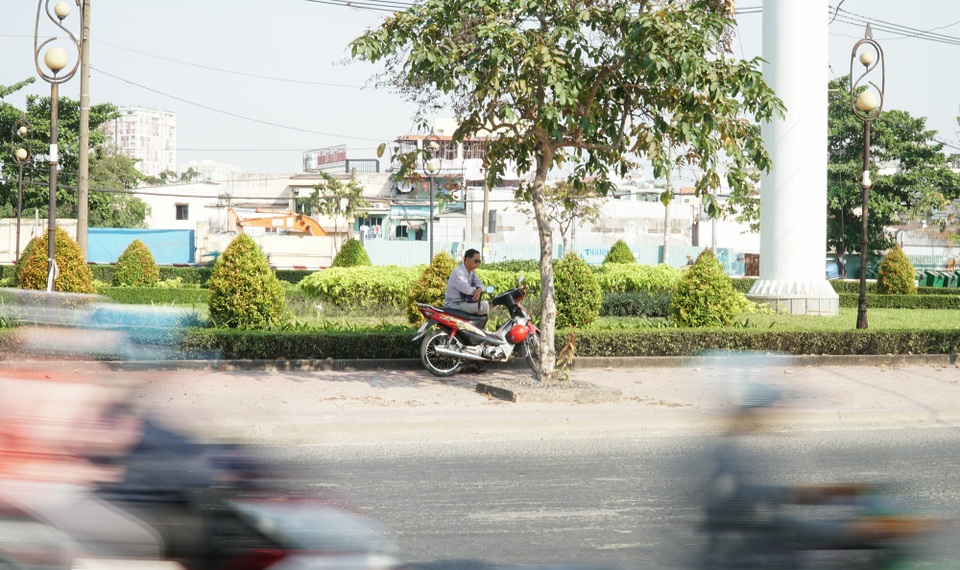 Sài Gòn nắng gay gắt, người dân xếp hàng chờ mua nước giải nhiệt - 2 Một tài xế xe ôm núp mình dưới bóng cây để chờ khách