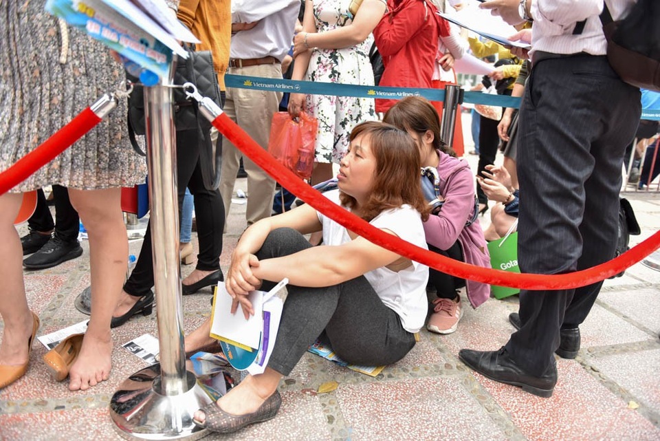 Một người phụ nữ mệt mỏi ngồi nghỉ chân chờ đến lượt mua vé máy bay.