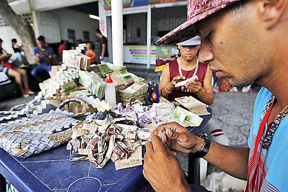 Tiền giấy Venezuela vô giá trị, dân dùng làm giấy gấp thủ công - 1 Anh Richard Segovia ngồi gấp thủ công với các loại tiền giấy của Venezuela. (Nguồn: Borneo Bulletin)