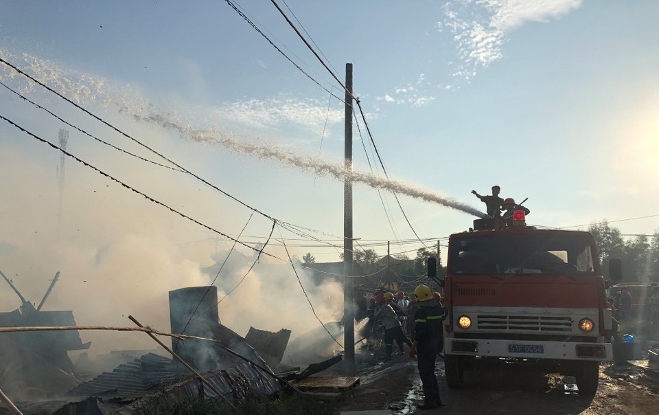 Cảnh sát chữa cháy phun nước để chống cháy lan sang các nhà dân cạnh khu lán trại bị cháy rụi.