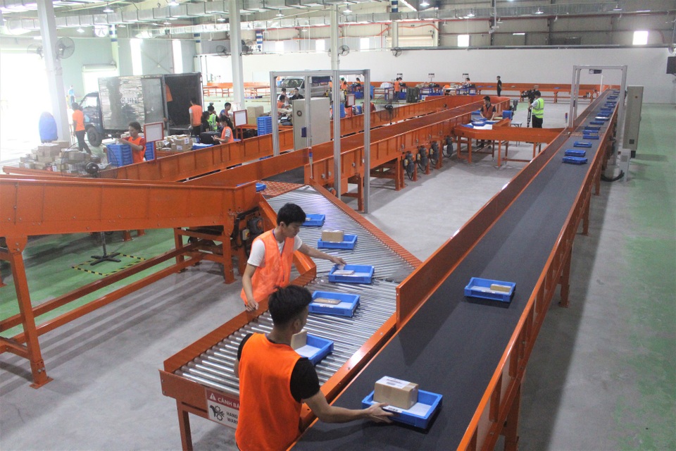 Ông Vũ Đức Thịnh: “Tiên phong trong khâu hậu cần thương mại điện tử” - 2 Nhân viên làm việc trong hệ thống phân loại hàng hóa tự động của Lazada với robot tự phân loại hàng hóa theo kích thước và mã vạch. (Ảnh: Cẩm Vy)