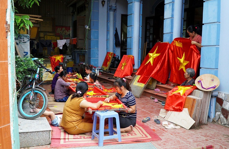 Những bàn tay tài hoa giữ nghề thêu cờ Tổ quốc - 1
Khung cảnh làm việc tất bật của những người thợ thủ công tại hộ gia đình chị Vương Thị Nhung ở làng Từ Vân - làng có nghề truyền thống may thêu cờ Tổ quốc.