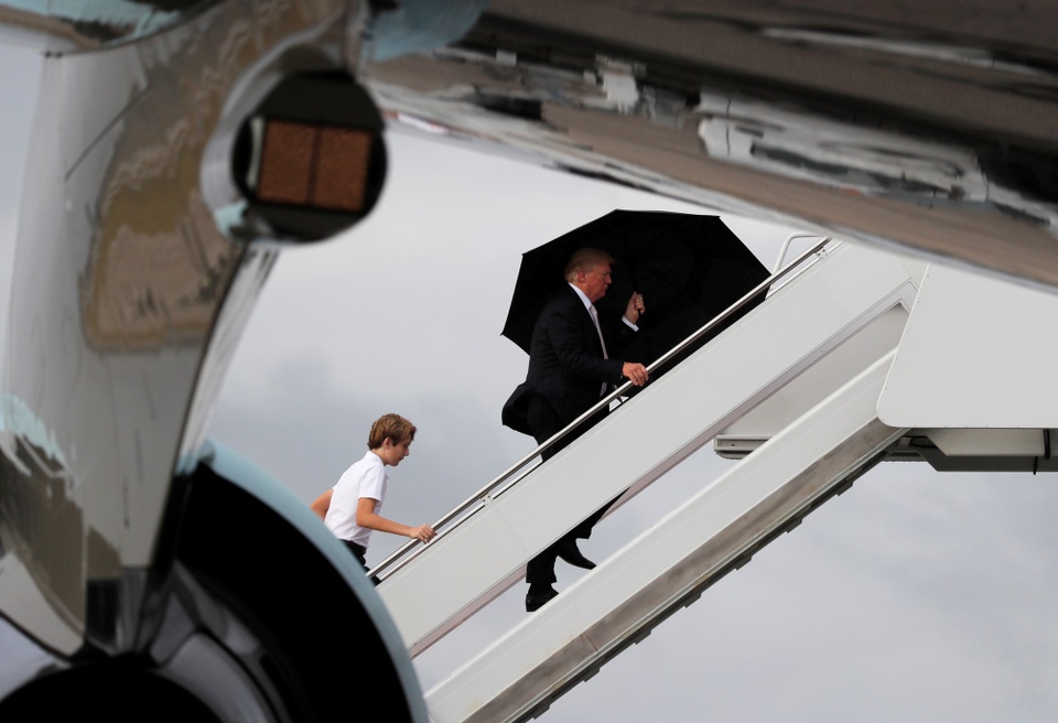 Tổng thống Trump che ô một mình, phu nhân và con trai đầu trần - 2 Kết thúc kỳ nghỉ, Tổng thống Trump cùng vợ và con trai lên chuyên cơ Không Lực Một để trở lại thủ đô Washington. Khi đó trời đổ mưa và ông Trump được nhìn thấy mang theo một chiếc ô lớn màu đen. (Ảnh: Reuters)