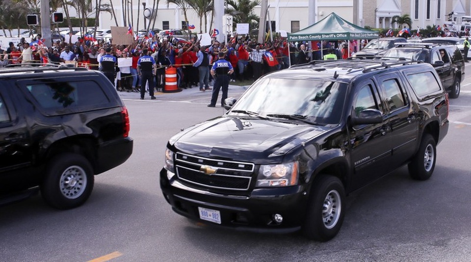Tổng thống Trump che ô một mình, phu nhân và con trai đầu trần - 8 Haiti, El Salvador và Liên minh châu Phi (AU) đều đồng loạt công kích Tổng thống Trump, đồng thời kêu gọi ông đưa ra lời xin lỗi chính thức. Tuy nhiên nhà lãnh đạo Mỹ khẳng định ông không nói bất kỳ điều gì miệt thị người dân của các quốc gia này. Trong ảnh: Người biểu tình tập trung phản đối Tổng thống Trump khi đoàn xe chở ông đi qua. (Ảnh: Palm Beach Post)