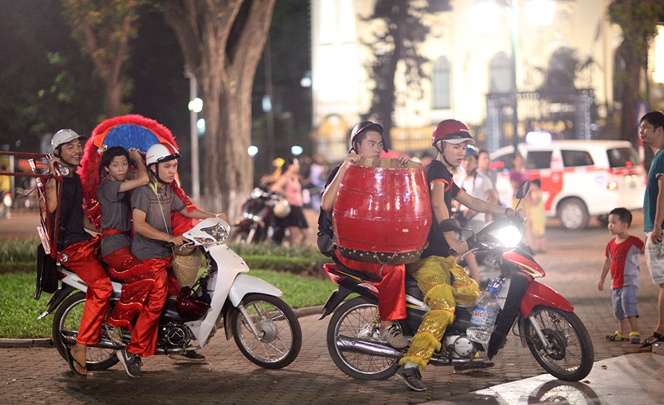 
Một nhóm múa lân vừa kết thúc phần biểu diễn tại vườn hoa Lý Thái Tổ đã vội vàng di chuyển đến địa điểm khác. Một số thành viên trong đoàn không đội mũ bảo hiểm và vận chuyển các đạo cụ khá cồng kềnh.
