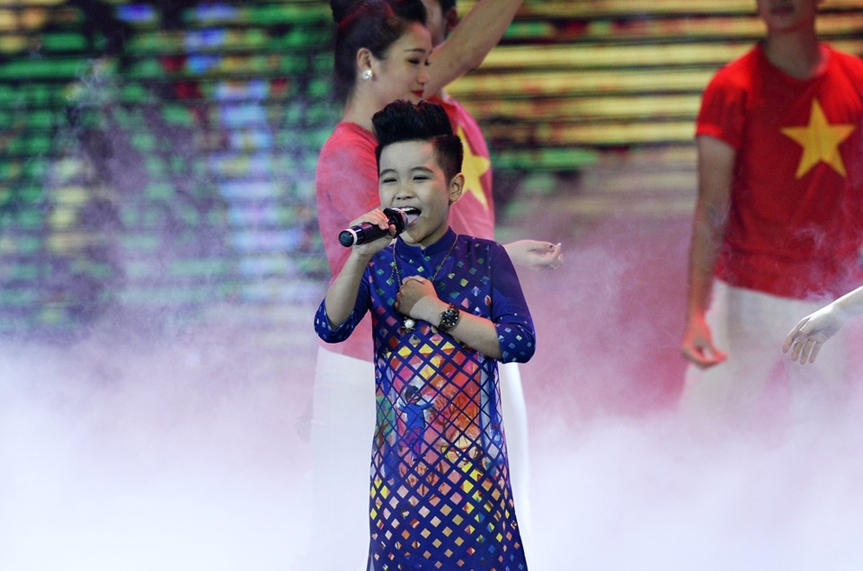 Bé Nhật Minh lại chọn một chiếc áo dài với sắc xanh, đỏ vàng đan xen để phù hợp với không khí tươi vui và tinh thần của ca khúc.