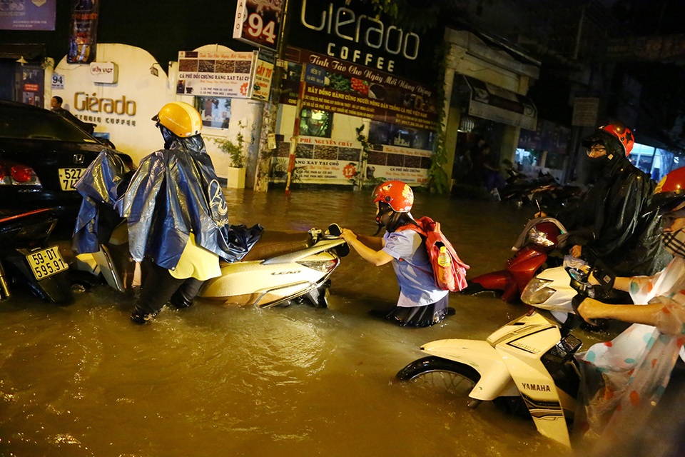 
Cháu bé tối muộn vẫn chưa được về nhà sau giờ học, hì hục giúp mẹ đẩy xe qua đoạn đường ngập sâu.
