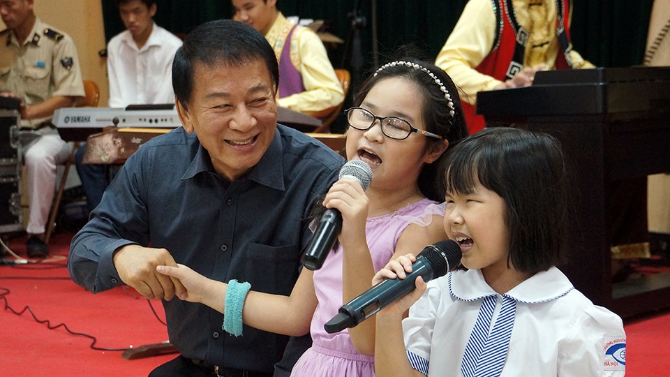 
Đại sứ Hữu nghị Ryotaro Sugi nắm tay các em nhỏ đang trình diễn bài hát Chiếc đèn ông sao.
