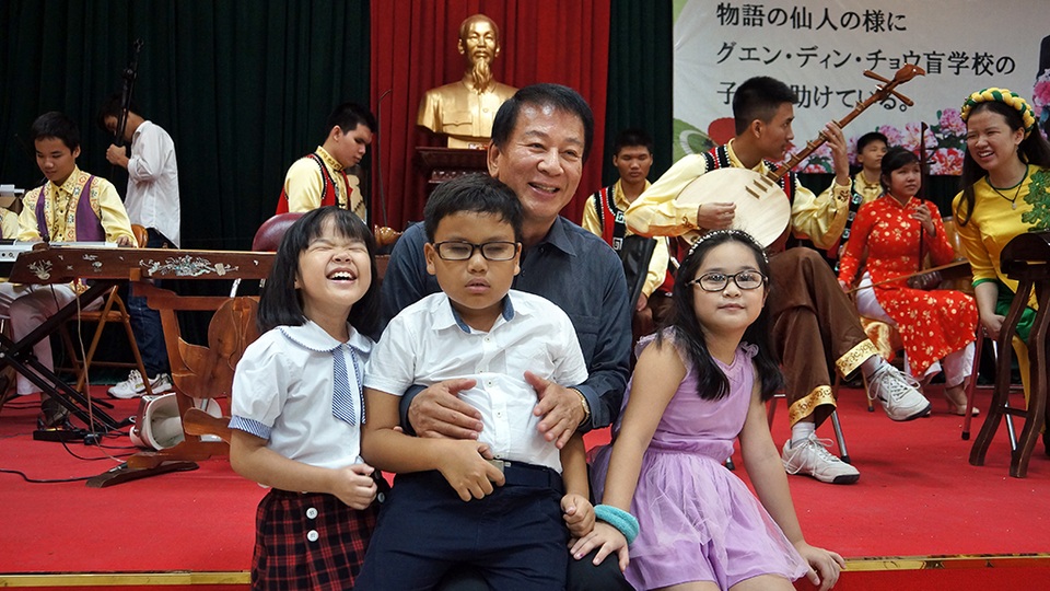
Đại sứ Sugi thận thiện ôm các cháu nhỏ vào lòng và vui đùa.
