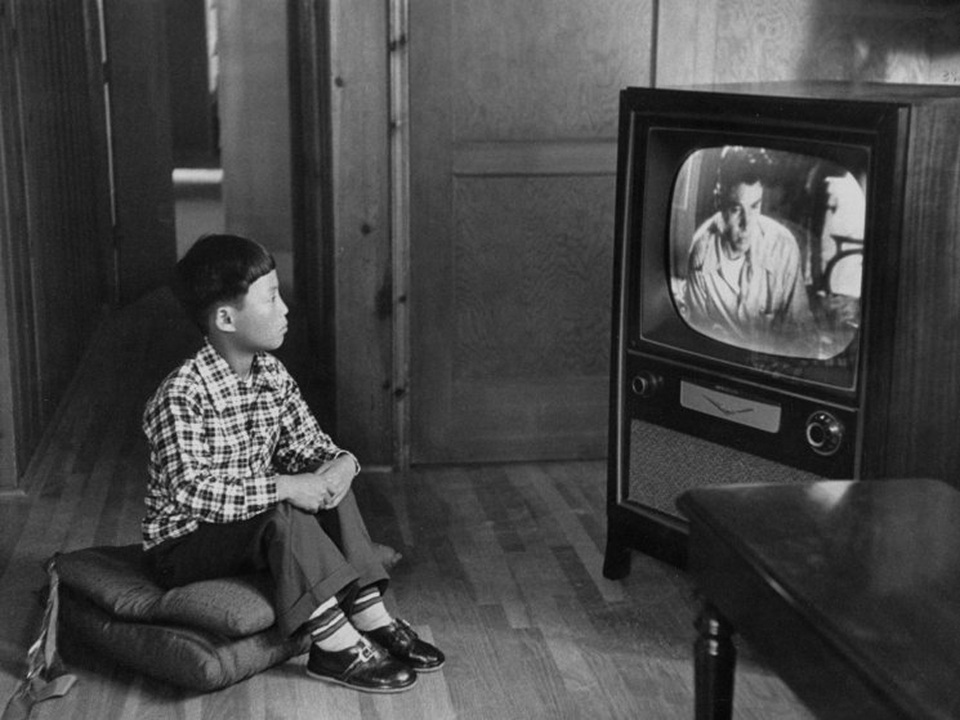 Cậu bé gốc Hàn Kang Koo Ri đang ngồi xem TV trong gia đình bố mẹ nuôi ở Los Angeles. Ảnh chụp năm 1956.