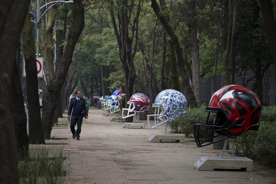 Người đi bộ đi ngang qua một sắp đặt nghệ thuật khổng lồ khắc họa những chiếc mũ của các cầu thủ bóng bầu dục. Ảnh chụp ở thành phố Mexico.