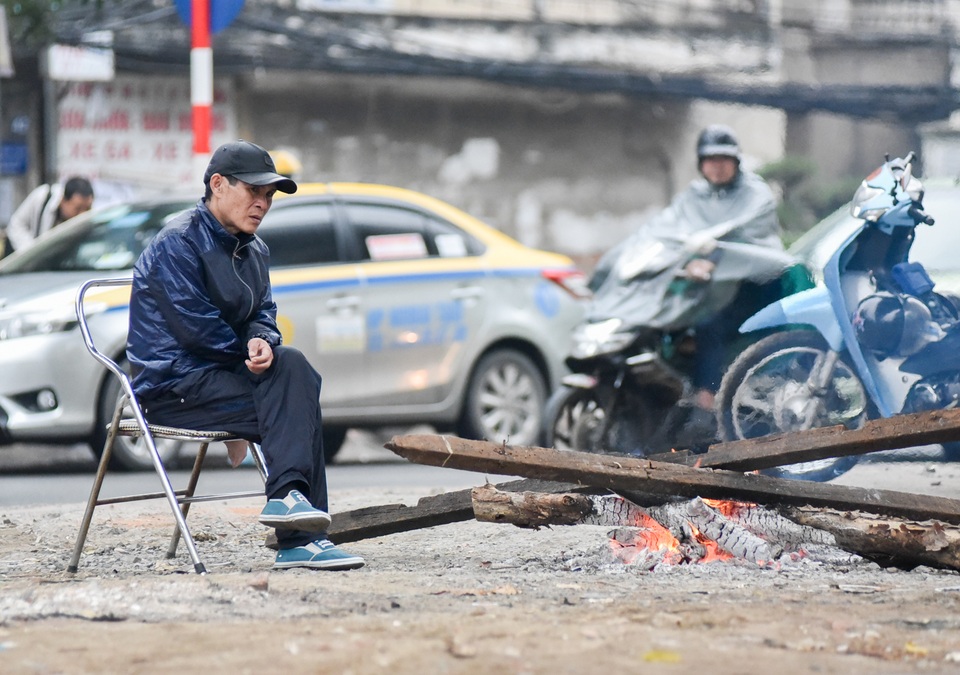 Người dân Hà Nội đốt củi sưởi ấm trên đường trong ngày mưa rét - 7 Mưa ngày càng dày, một người trông xe trên đường Hào Nam (Quận Ba Đình, Hà Nội) dùng những thanh gỗ lớn để đốt sưởi.