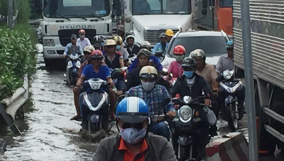 
Xe máy chen chút giữa dòng xe tải, container...trong khi mặt đường xuống cấp nghiêm trọng, ngập nước, đất đá lởm chởm.
