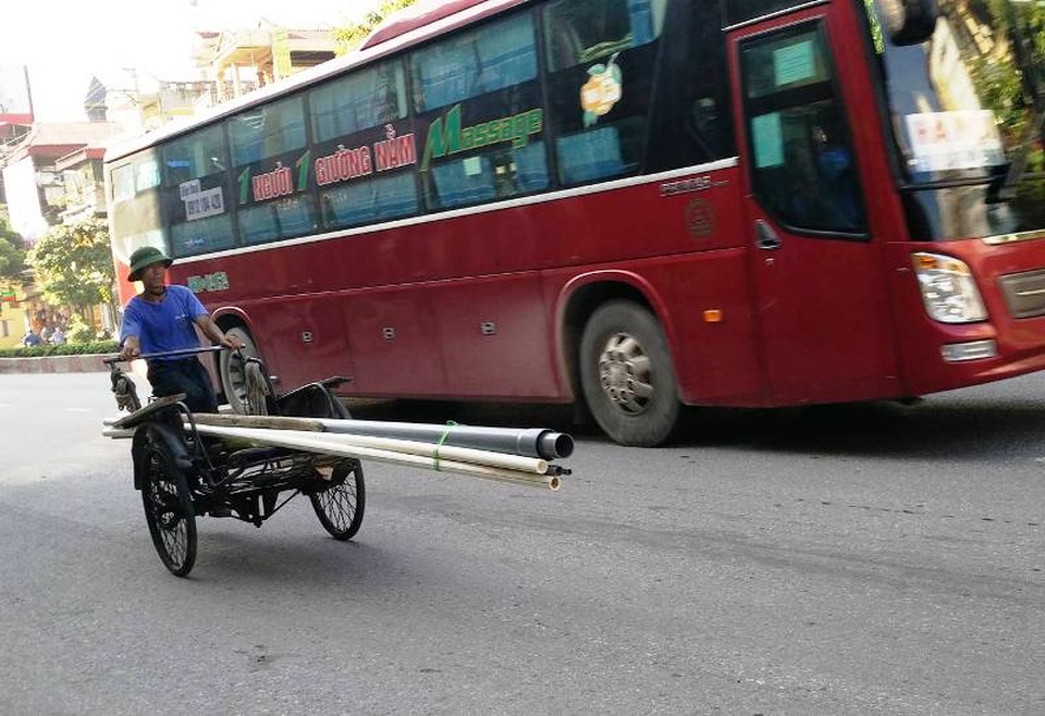 Một chiếc xe xích lô chở hàng dài ngang với xe khách giường nằm.