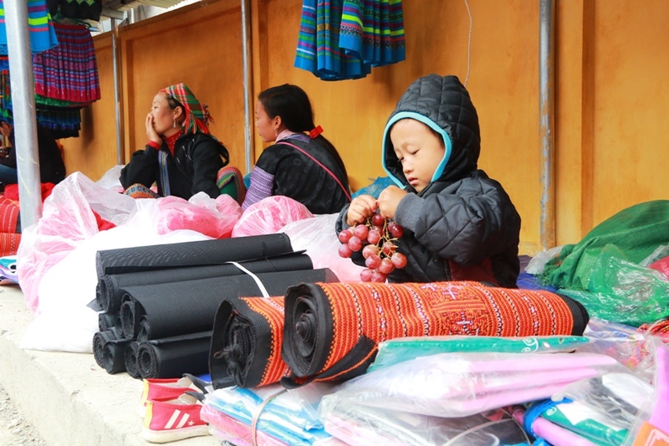 Em bé đến chợ bán hàng cùng mẹ được trả thù lao bằng một chùm nho, đang chọn lựa từng quả để ăn.